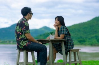 Asian couple are sitting on chair with table on mountain and river background with smile face