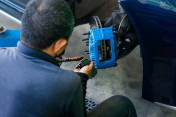 Bangkok, Thailand - January 16, 2022 : Unidentified car mechanic or serviceman disassembly and checking a disc brake and asbestos brake pads for fix and repair problem at car garage or repair shop. Checking car brake system for repair at car garage