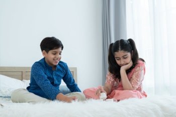 Happy Indian family, brother and sister with traditional clothes playing fun game together, teenage boy and girl sitting on bed at home, sibling relationship concept
