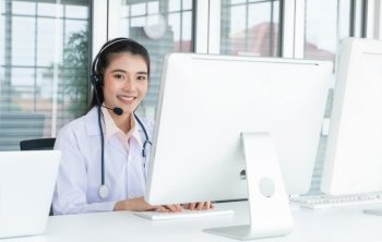 Portrait of Asian female doctor with headsets and stethoscope, using computer advice medicines or medical treatment to patient. Online telemedical service from hospital clinic. Look at camera, smiling
