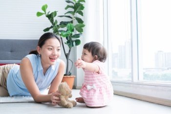 Asian beautiful young mother and Caucasian 7 months baby newborn girl playing with Bear doll toy. Single mom lying on floor smiling playing with little daughter in living room at home. Family bonding