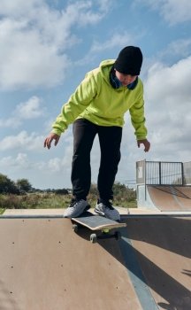 young, teenager, with a skateboard, diving down the slope, on a rink, skateboarding, wearing headphones, green sweatshirt, black hat, swinging, on a sunny day. young, teenager, with a skateboard, diving down the slope, on a rink, skateboarding,