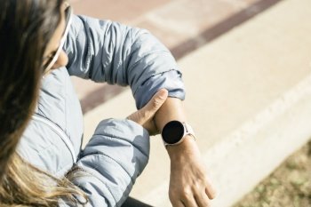 This stock photo shows a young Latina woman focused on her smart watch as she checks her heart rate. The image reflects the woman’s commitment to her well-being and her interest in technology as a tool for monitoring her health. The blurred background highlights her figure, while the natural light accentuates her natural beauty. This image would be perfect for illustrating articles or posts related to personal care and technology in health.. Latina Woman Checking Heart Rate on Smart Watch