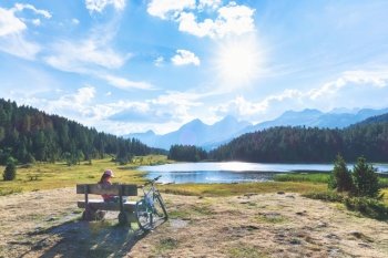 Girl rests during bike ride near a mountain lake in the Swiss alps
