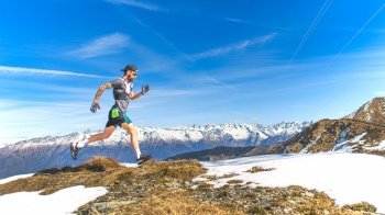 A male mountain runner trains on grass and snow