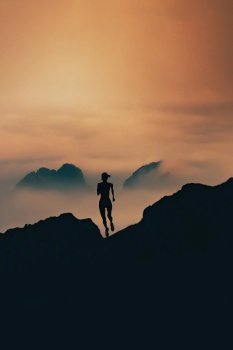 Woman runs in silhouette through the mountains at sunset