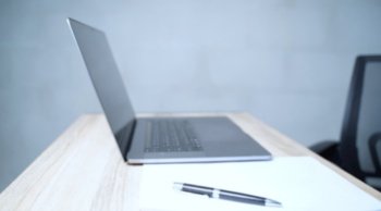 Abstract blurred image of a bright wooden desk with pen and paper and a laptop.
