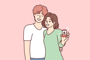 Young couple of man and woman stand in embrace and look at camera showing box with wedding ring. Bride and groom in casual clothes after proposal for joint family life. Flat vector illustration. Young couple of man and woman stand in embrace showing box with wedding ring. Vector image