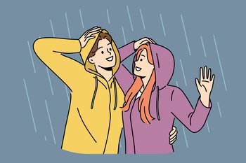 Happy couple stands in rain in waterproof hoods and hugs rejoicing at cloudy weather and first autumn downpour. Cheerful man and woman walking in rain during date or having romantic conversation. Happy couple stands in rain in hoods and hugs rejoicing at cloudy weather and autumn downpour