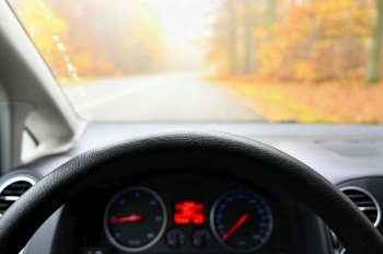 Car interior with dashboard on wet road in autumn season. Foggy and dangerous driving - concept for traffic and road safety - view from the driver’s seat.