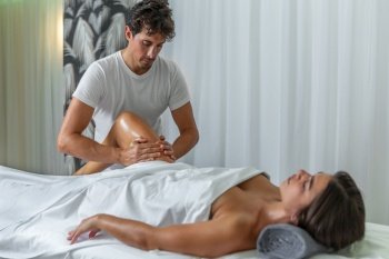 Male therapist giving a leg massage to latina woman in a spa salon. Spa concept.. Male therapist giving a leg massage to adult woman in a spa salon