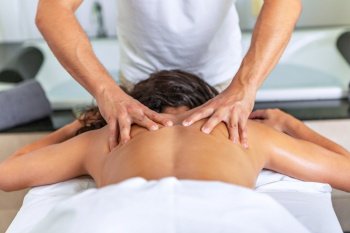 Close rear view of relaxing woman lying face down on massage table receiving a back massage at spa center. Concept of spa.. Rear view of relaxing woman lying face down on massage table receiving a back massage