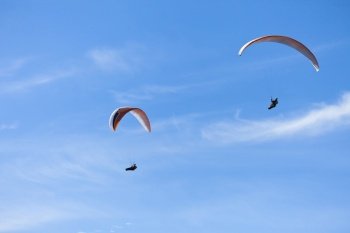 Two paragliders on parachutes flying in blue sky.. Two paragliders in the air