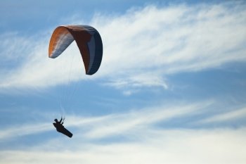 Side view of paraglider?flying in blue cloudy sky.. Parachutist in the air