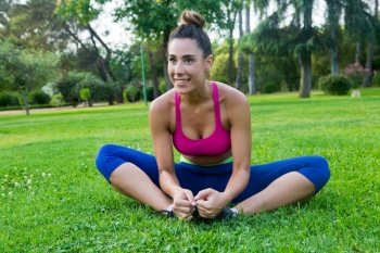 Portrait of smiling sportswoman in bright sportswear stretching in park on grass