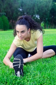 Portrait of beautiful sportswoman stretching on grass in park.Bokeh