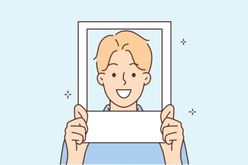 Smiling man holds photo near face and poses for picture on avatar in social network. Positive guy teen participates in photo shoot with props to create professional model portfolio.. Smiling man holds photo near face and poses for picture on avatar in social network