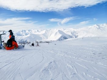 Ski slope. Snowboarder sits on snow. Winter sport. Ski resort of Georgia Gudauri. Snowy slope and mountains. Ski slope. Snowboarder sits on snow