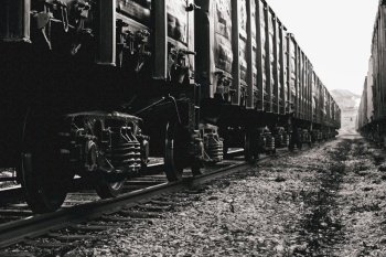 Freight wagons closeup on rails. Stylized black and white photo. A long train, many pairs of wheels with springs.