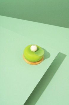 A freshly baked pastry with green and white icing, sitting atop a green-hued surface. A green pastry with white icing sitting on top of a green surface