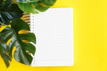 Top view of blank note paper and monstera leaf on yellow background.. Top view of blank note paper and monstera leaf on yellow background