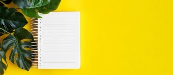 Top view of blank note paper and monstera leaf on yellow background. banner. Top view of blank note paper and monstera leaf on yellow background