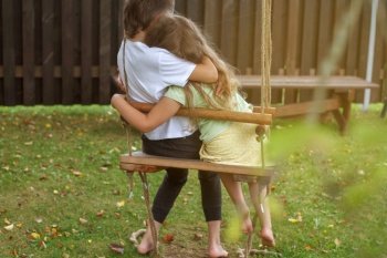children sitting on a swing in the garden. older brother hugging little sister.. children sitting on a swing in the garden. older brother hugging little sister