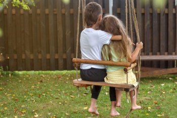 children sitting on a swing in the garden. older brother hugging little sister.. children sitting on a swing in the garden. older brother hugging little sister