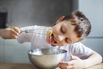 Child cooking at the kitchen. boy stirring dough for a cake in the steel bowl. the kid tastes food and licks a whisk. Child cooking at the kitchen. boy stirring dough for a cake in the steel bowl. kid tastes food and licks a whisk
