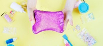 Making slime at home. child holding and stretching colorful slime. DIY concept.Kids hands make purple slime with sequins on a yellow background. Flat lay, top view. banner. Making slime at home. child stretching colorful slime. DIY concept. hands make slime with sequins on yellow background