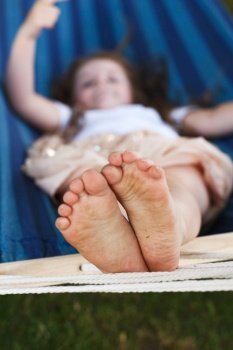 closeup of little girl’s feet relaxing in the blue hammock during her summer vacation in the back yard. closeup of little girl’s feet relaxing in the blue hammock during her summer vacation in back yard