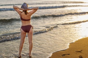 Back view of a woman in bikini standing on a sandy beach, relax and enjoy holiday . Girl watch beautiful sunset. Summer vacation.. Back view of a woman in bikini standing on a sandy beach. Girl watch beautiful sunset. Summer vacation.