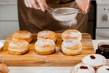 Woman chef prepares fresh donuts in her bakery. Cooking traditional Jewish Hanukkah Sufganiyot. Small business concept. Hands sprinkle Berliners with powdered sugar.. Woman chef prepares fresh donuts in her bakery. Cooking traditional Jewish Hanukkah Sufganiyot. Small business concept. 