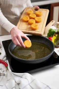 Woman puts cheese balls into frying pan with hot cooking oil.. Woman puts cheese balls into frying pan with hot cooking oil