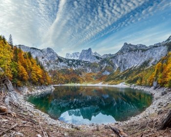 Tree stumps after deforestation near Hinterer Gosausee lake, Upper Austria. Colorful autumn alpine mountain lake  view with clear transparent water and reflections. Dachstein summit and glacier in far