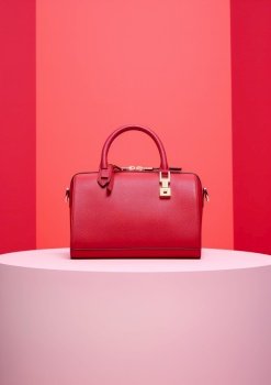 red handbag on a white podium and pink background