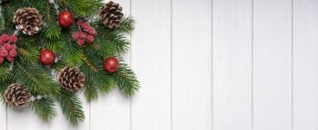 Christmas tree branch decorated with red balls, fir cones and berries on white wooden background. Top view, flat lay with copy space, banner, header, New Year background