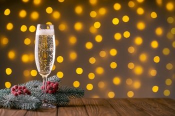 Wine glass with bubbly champagne and fir branch with decor on background of blurry sparkling lights. Happy New Year holiday greeting card, banner, header with copy space 