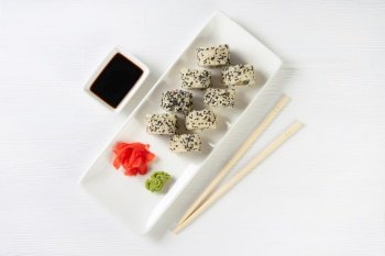 Sushi roll California with salmon, sesame seeds, avocado, cream cheese on white background. Sushi menu, rolls served on white dish with wasabi, ginger and soy sauce. Japanese cuisine food.. Sushi roll California with salmon, sesame seeds, avocado, cream cheese on white background
