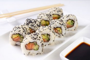 Sushi roll California with salmon, sesame seeds, avocado, cream cheese on white background. Sushi menu, rolls served on white dish and soy sauce. Traditional Japanese cuisine food.. Sushi roll California with salmon, sesame seeds, avocado, cream cheese on white background