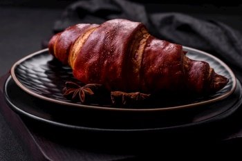Delicious crispy croissant with chocolate on a black ceramic plate on a dark concrete background