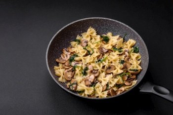 Delicious farfalle pasta with mushrooms, cheese and spinach with spices on a black plate on a dark concrete background