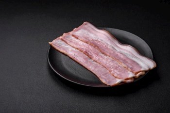 Delicious fresh bacon stripes with spices and salt on a dark concrete background