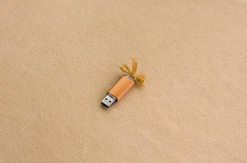 Orange usb flash memory card with a blue bow lies on a blanket of soft and furry light orange fleece fabric. Classic female gift design for a memory card