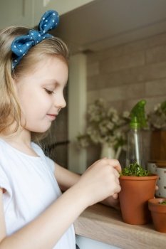 Little girl in her kitchen sitting and holding a pot of seedlings