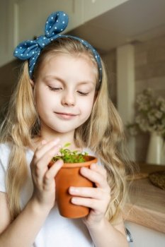 Little girl in her kitchen sitting and holding a pot of seedlings
