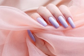 Girl’s hands with a soft purple manicure. Pink background of silk and tulle. Concept of beauty and care.