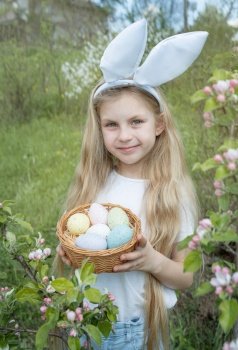 Cute little child wearing bunny ears on Easter day. Girl holding basket with painted eggs.
