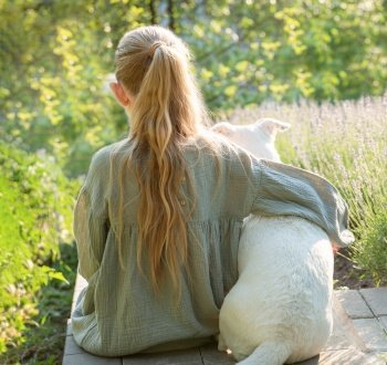 A little girl with a white dog sits and admires the lavender field. View from the back