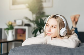 Young blonde woman in headphones listening to music and relaxing at home.